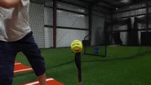 Indoor turf arena with sports equipment and a batter getting ready to hit a yellow ball
