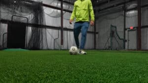 Indoor turf arena with sports equipment and netting with a person kicking a soccer ball