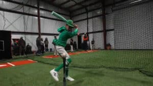 Indoor turf arena with sports equipment and netting with a young person hitting a baseball