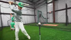 Indoor turf arena with sports equipment and netting with batter getting ready to hit a baseball