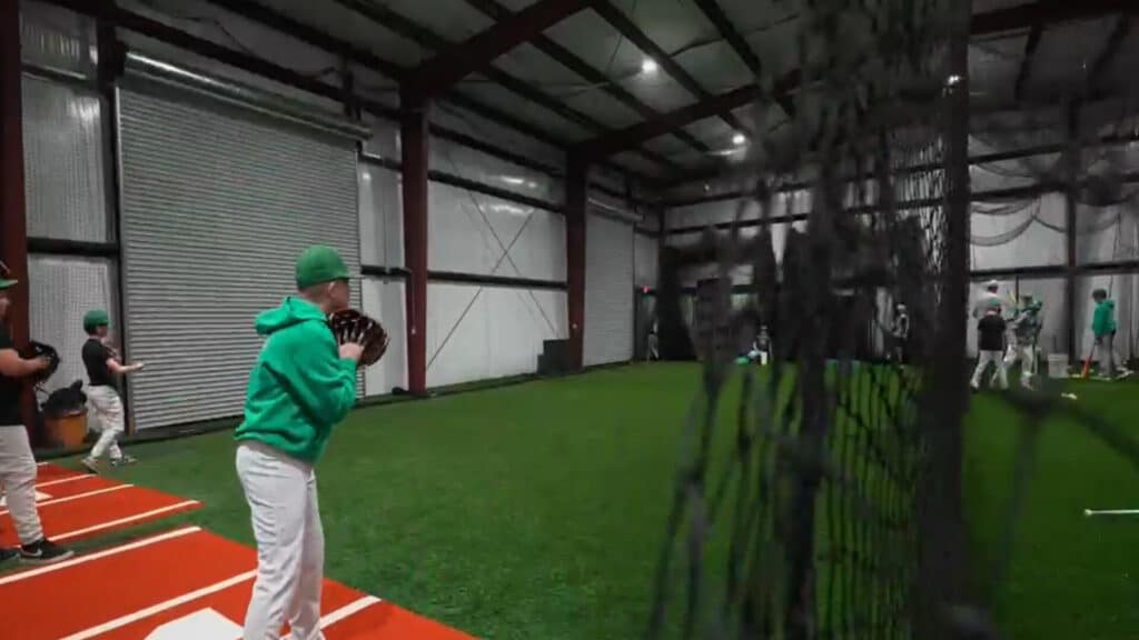 Indoor turf arena with sports equipment and netting with catcher catching a baseball
