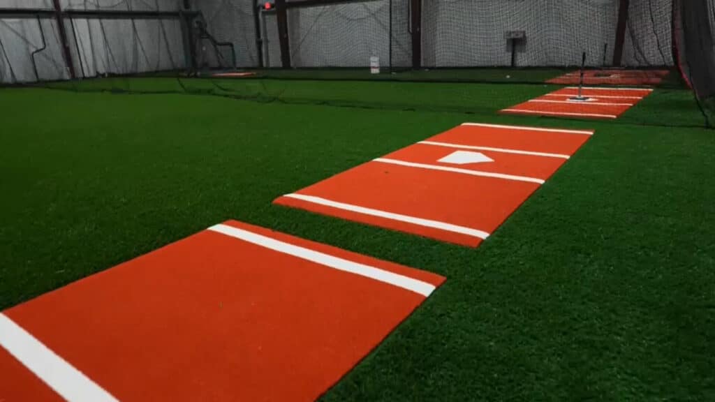 Indoor turf arena with sports equipment and netting with orange mounds for practicing baseball