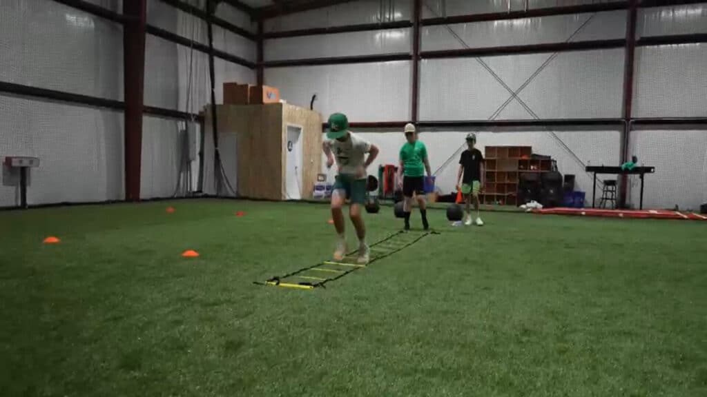 Indoor turf arena with sports equipment and netting with youth running up and down a floor ladder
