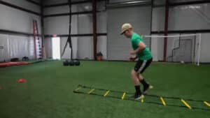 Indoor turf arena with sports equipment and netting with youth running up and down a ladder on the ground